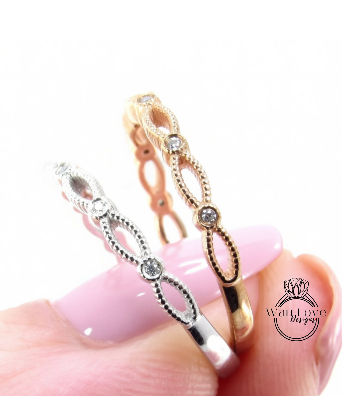 A close-up of a person's hand holding two rings with intricate designs and small diamonds.