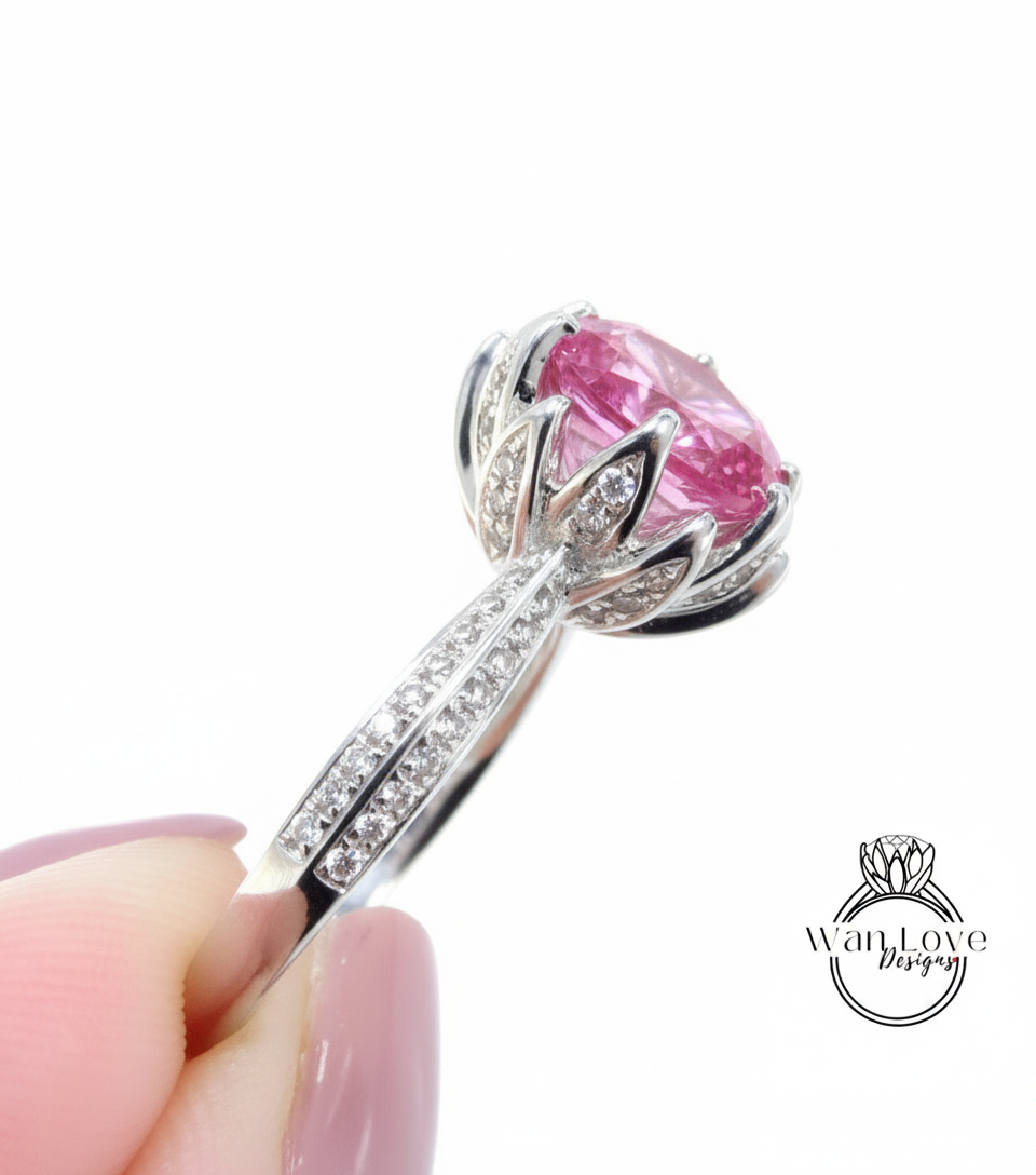 A close-up of a person's hand holding a silver ring with a large pink gemstone, likely a diamond.