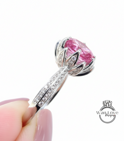 A close-up of a person's hand holding a silver ring with a large pink gemstone, likely a diamond.