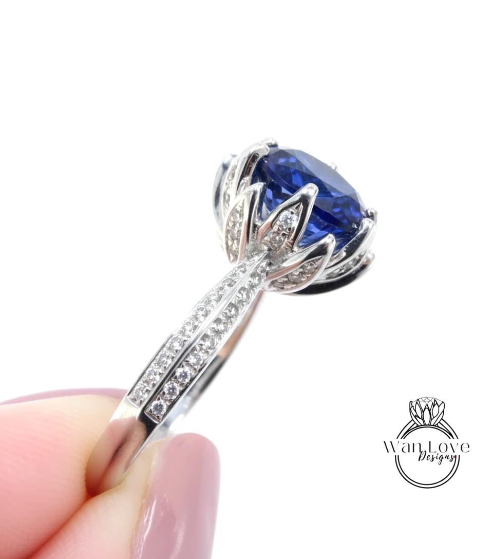 A close-up image of a person's hand holding a silver ring with a large blue gemstone, likely a sapphire, set in a decorative design.