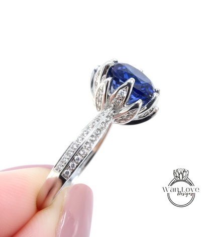 A close-up image of a person's hand holding a silver ring with a large blue gemstone, likely a sapphire, set in a decorative design.