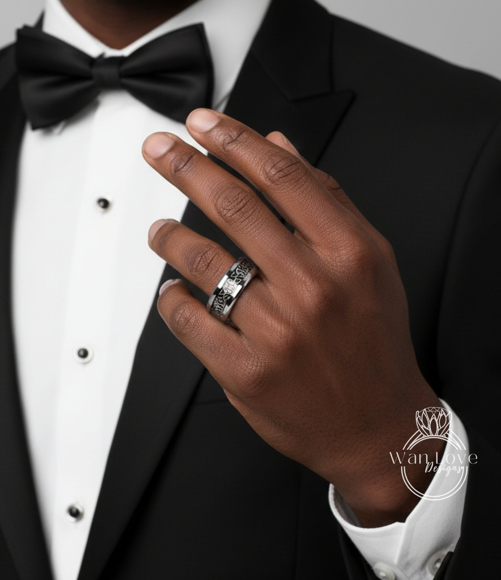 A close-up of a person's hand wearing a silver ring, with a black bow tie and a black suit jacket.
