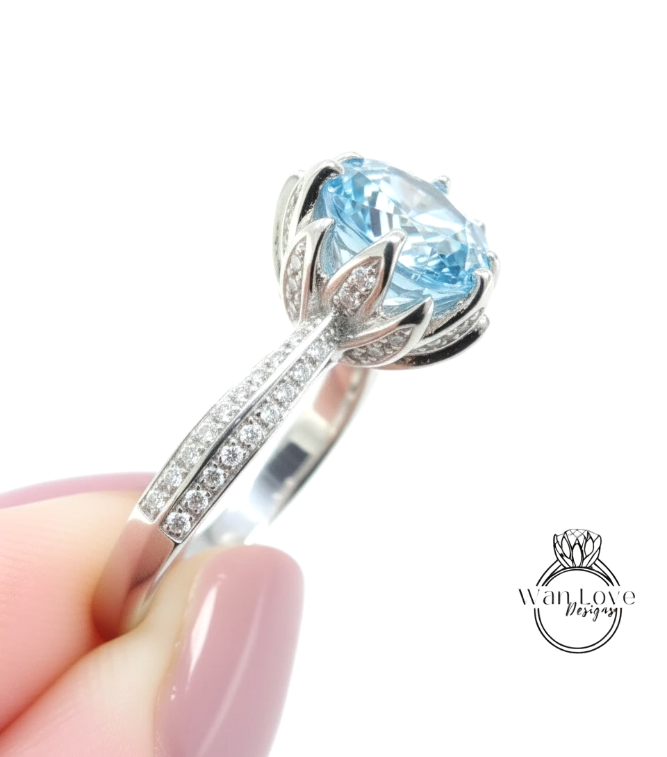 A close-up of a person's hand holding a silver ring with a large blue gemstone, likely an aquamarine or light blue gemstone.