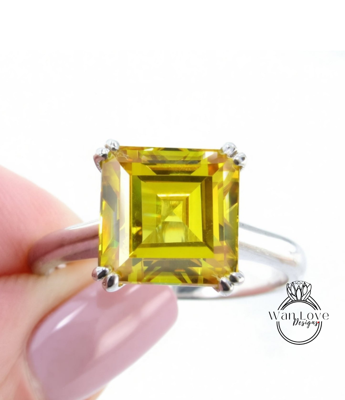 A close-up image of a person's hand holding a ring with a large, square-cut yellow gemstone.