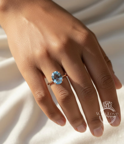 A close-up of a person's hand wearing a ring with a blue gemstone, likely an aquamarine or blue topaz stone.