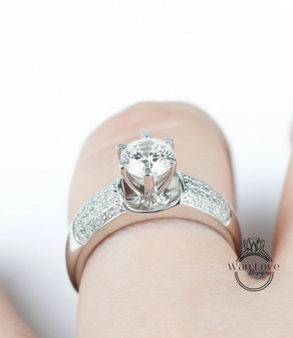 A close-up view of a person's hand wearing a diamond engagement ring with a large central diamond surrounded by smaller diamonds on the band.