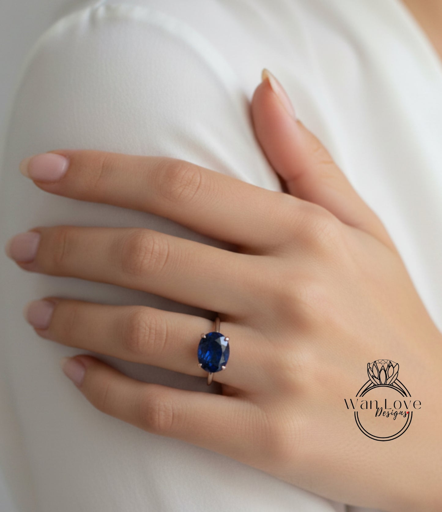 A close-up of a hand wearing a ring with a large blue gemstone, resting on a white surface.