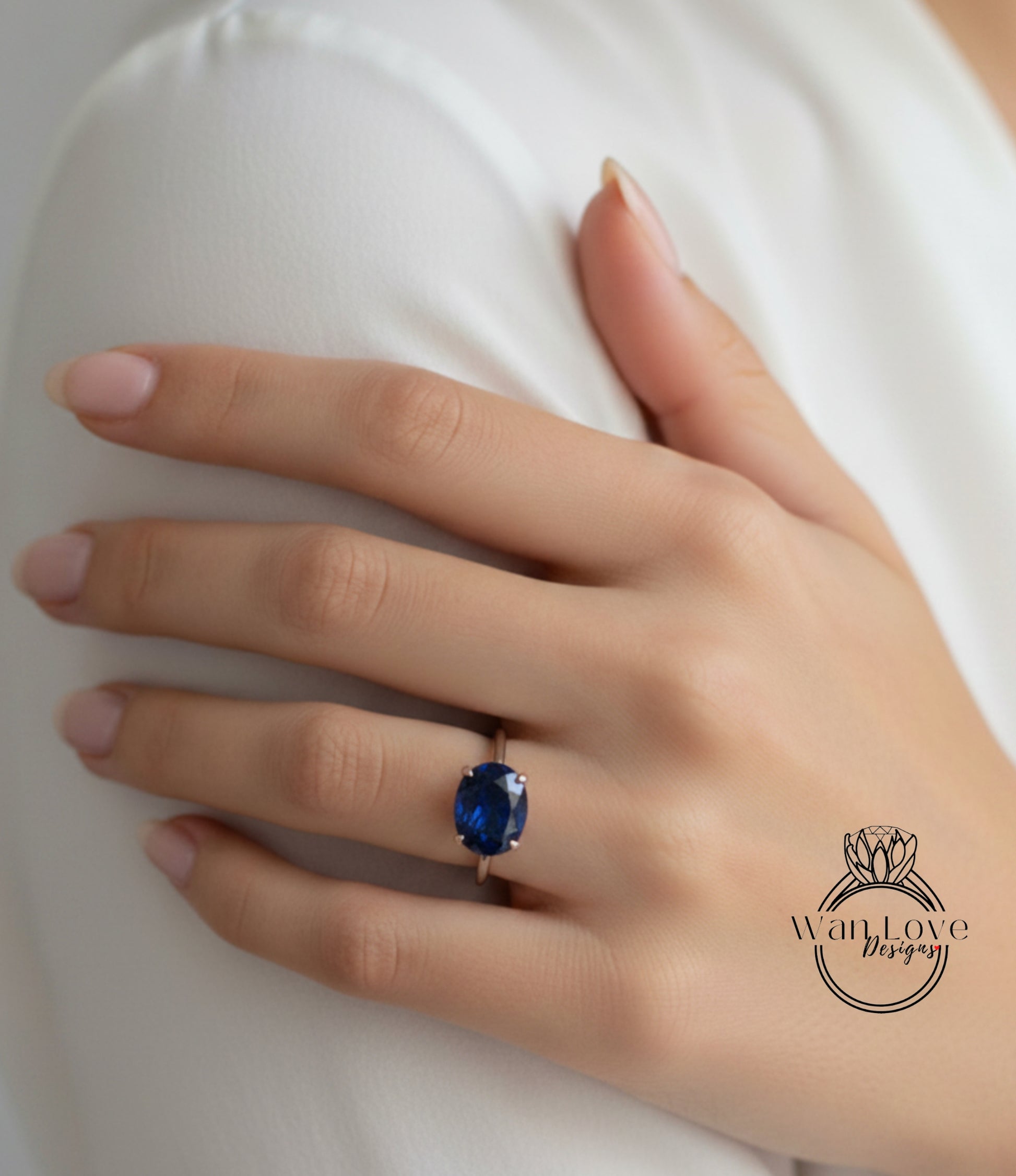 A close-up of a hand wearing a ring with a large blue gemstone, resting on a white surface.
