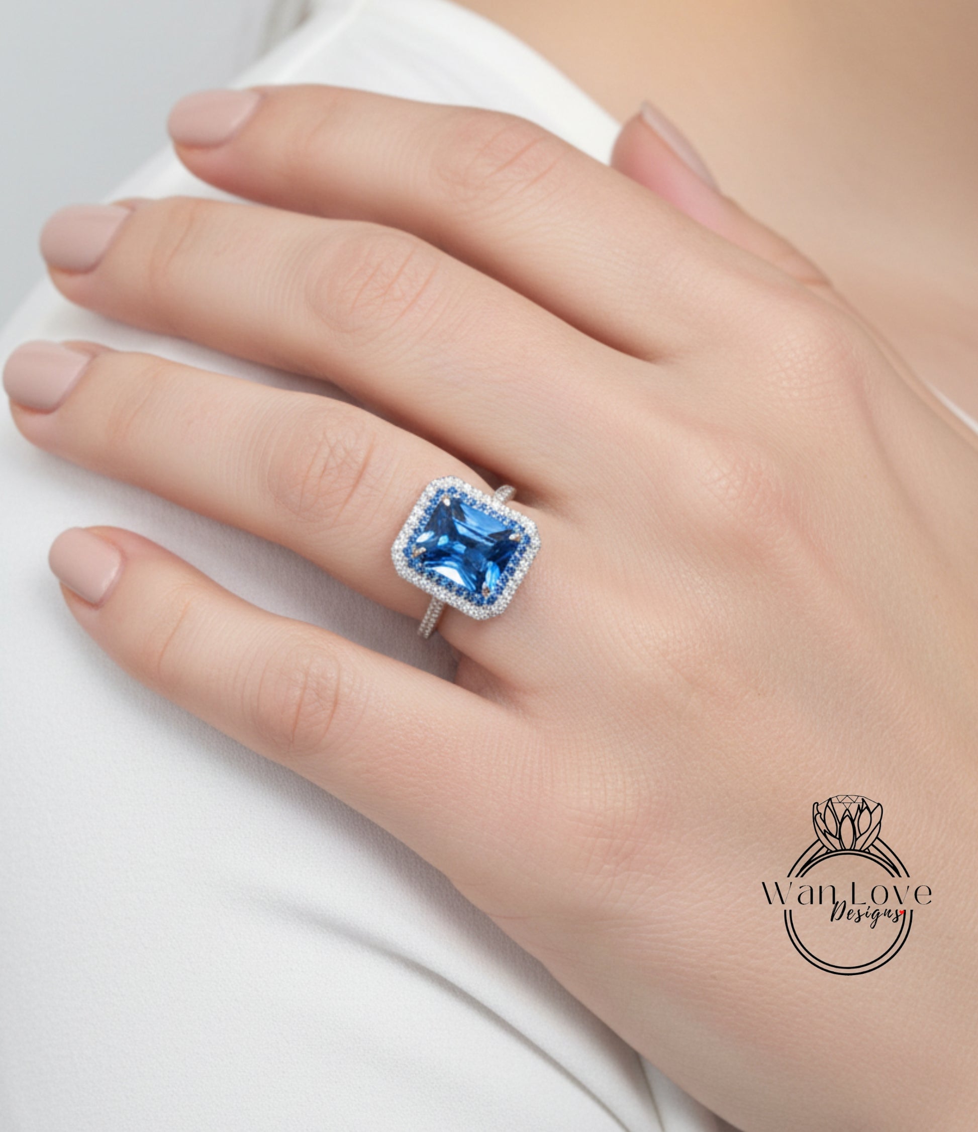 A close-up of a hand wearing a large blue gemstone ring with a halo of smaller diamonds around it.