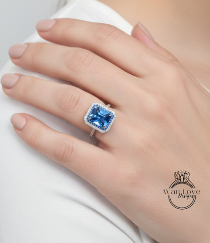 A close-up of a hand wearing a large blue gemstone ring with a halo of smaller diamonds around it.