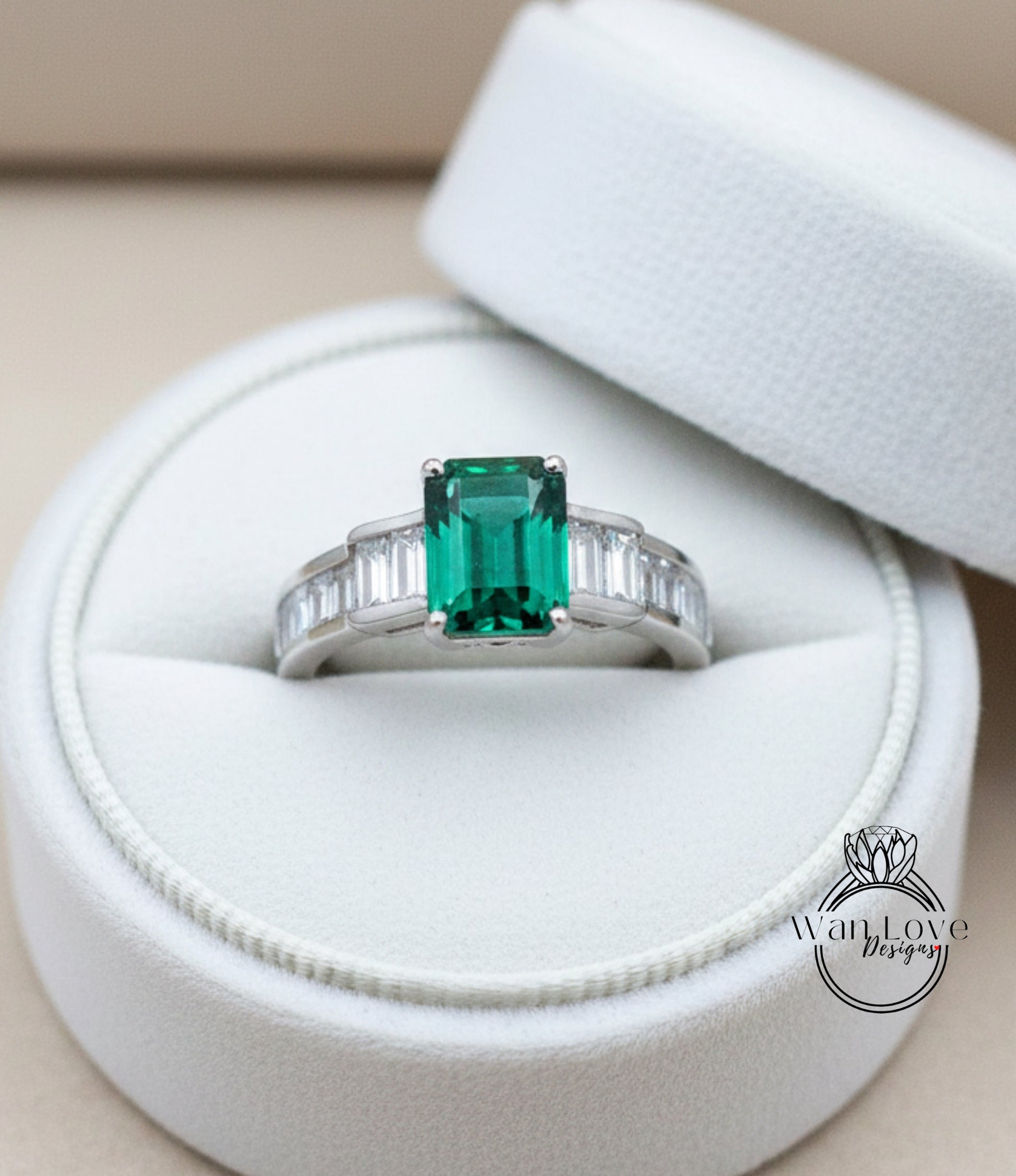 A white jewelry box containing a ring with a large, vibrant green gemstone.