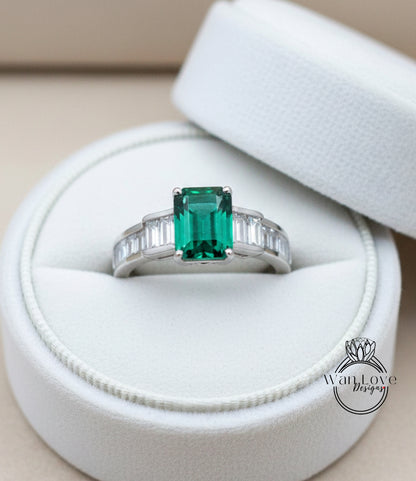 A white jewelry box containing a ring with a large, vibrant green gemstone.