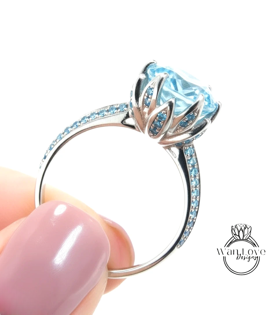 A close-up of a hand holding a silver ring with a large blue gemstone, likely a diamond, set in a decorative flower-like design.