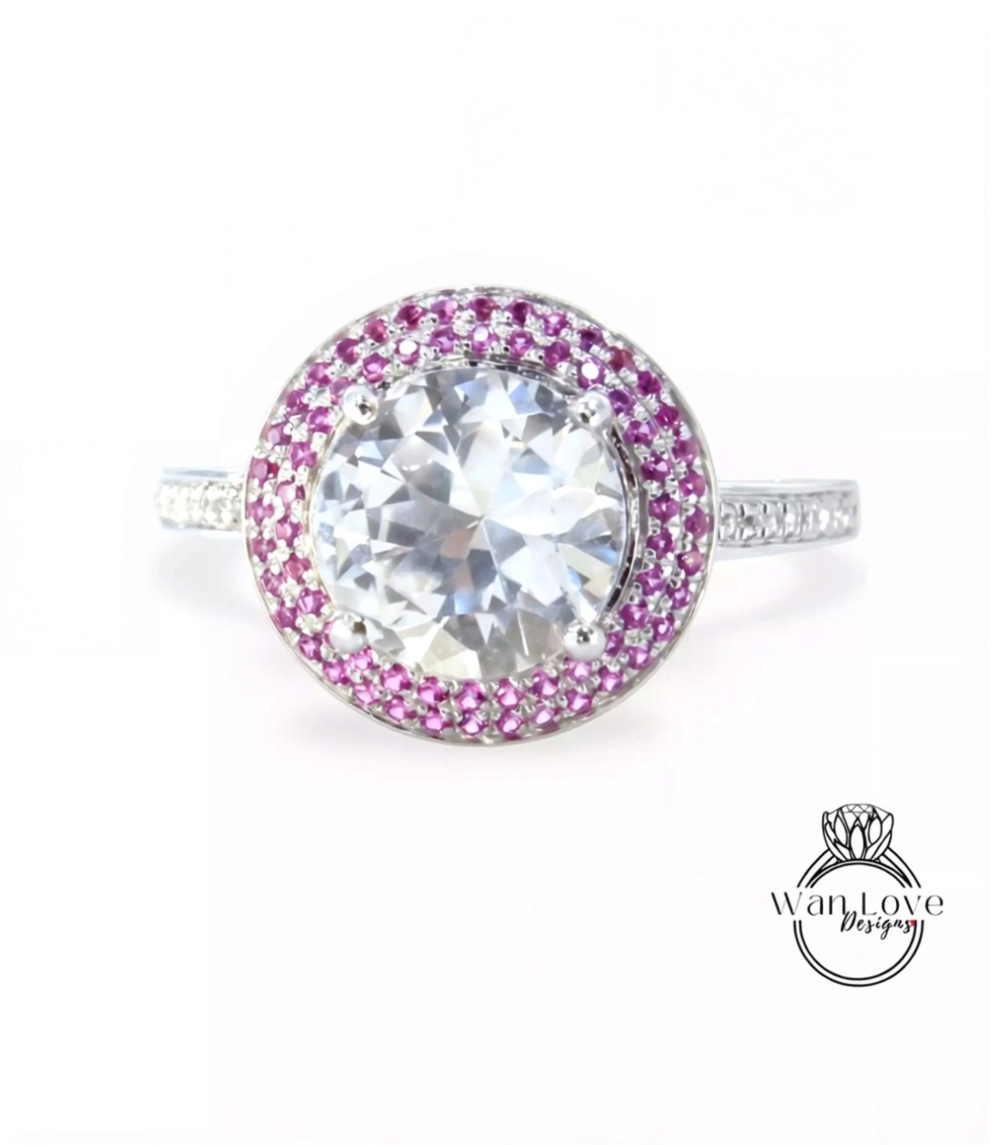 A large, round diamond ring with a halo of smaller diamonds around the center stone, set in a silver band with pink gemstones.