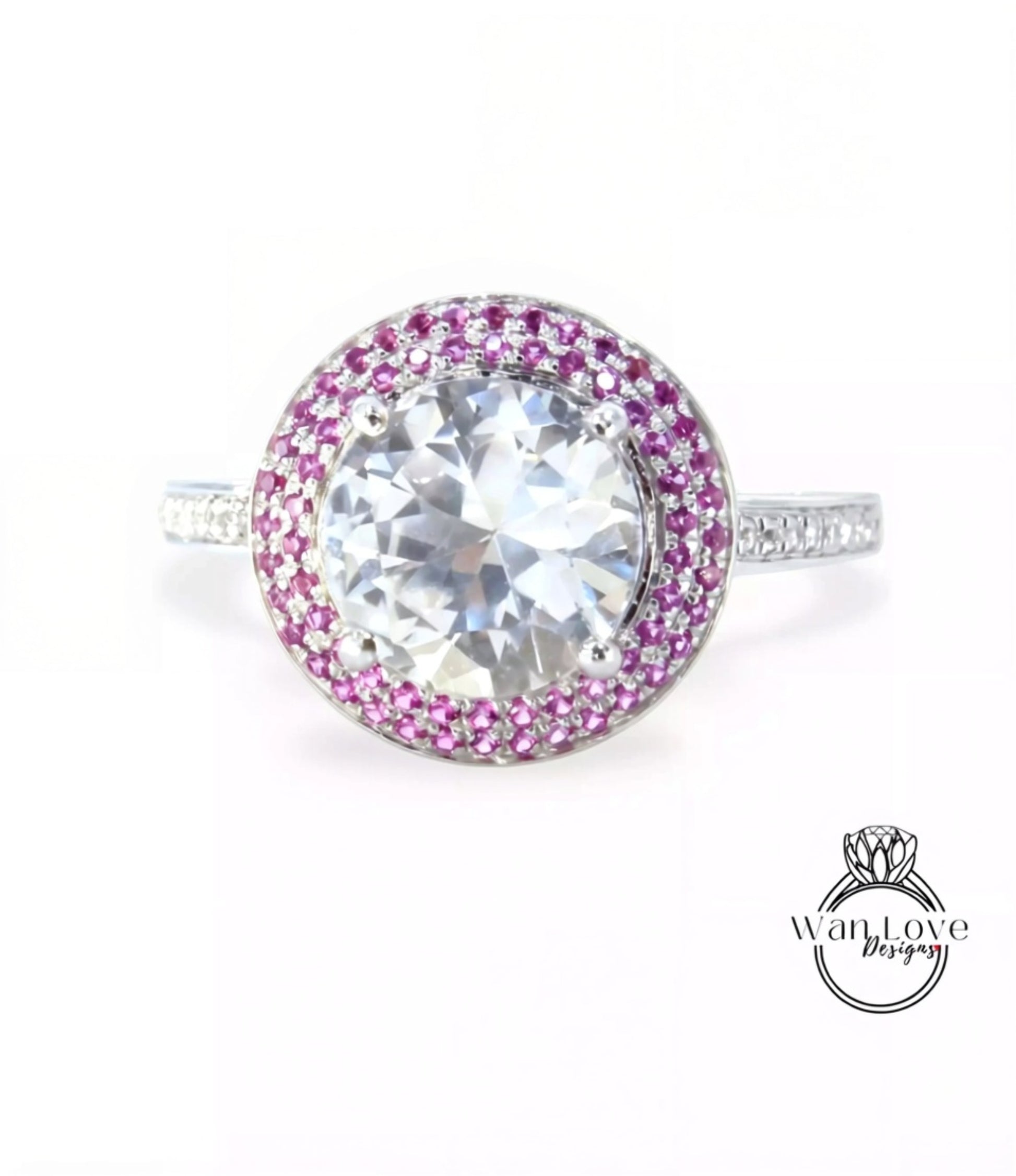 A large, round diamond ring with a halo of smaller diamonds around the center stone, set in a silver band with pink gemstones.