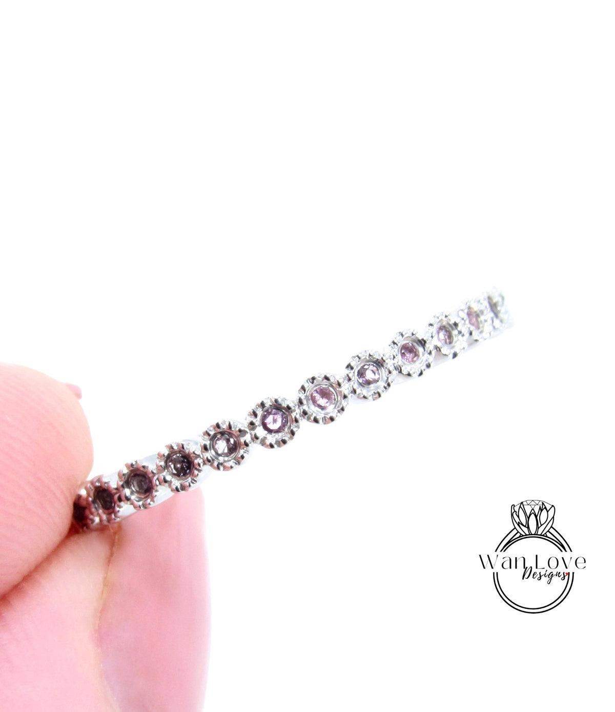 A close-up image of a person's hand holding a silver ring with a row of small, round, purple gemstones.