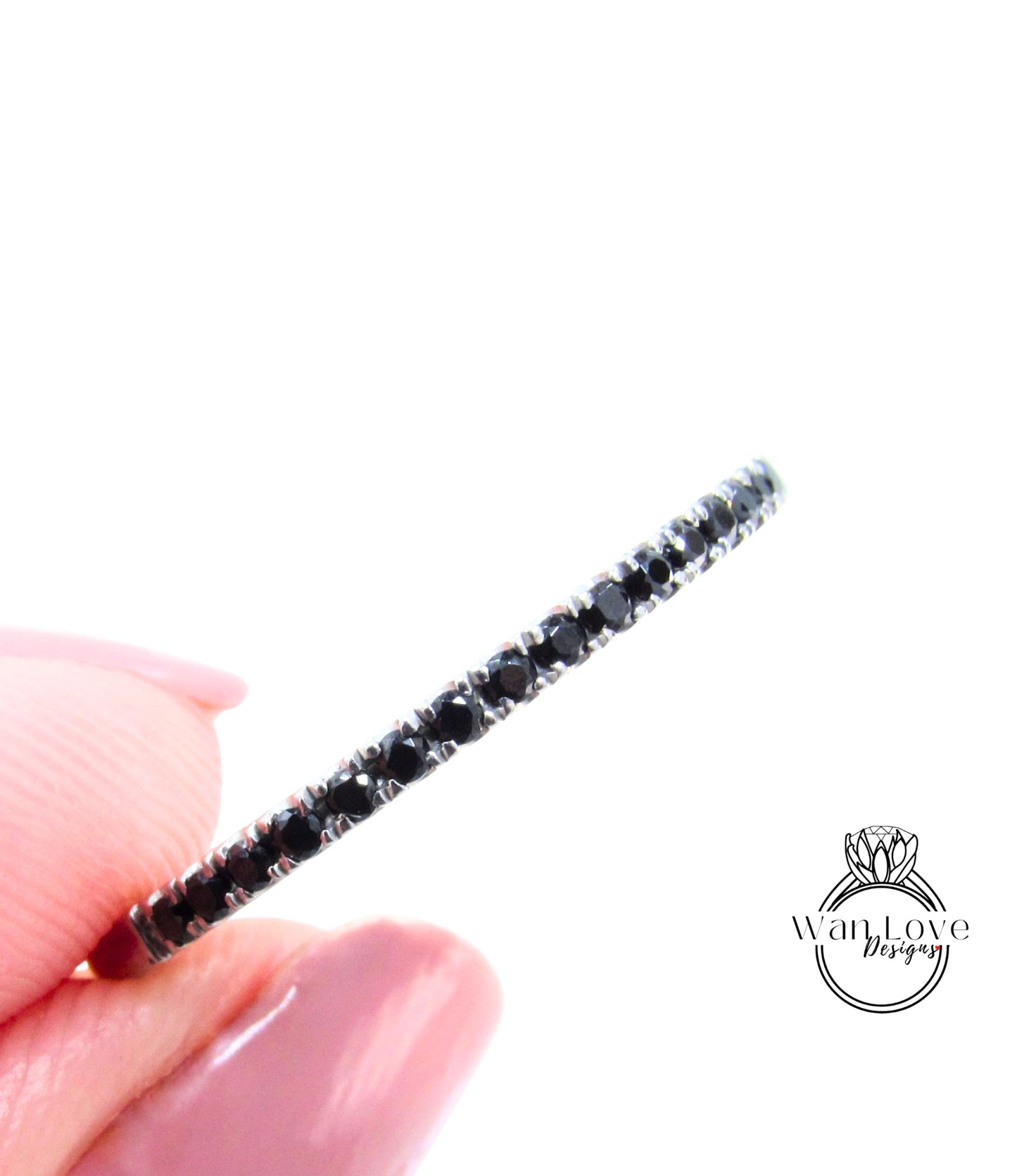 A close-up image of a person's hand holding a ring with a row of black gemstones.