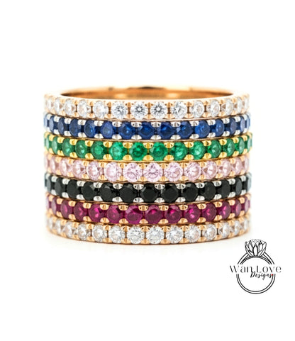 A stack of colorful gemstone rings with various colored gemstones set in a gold band.