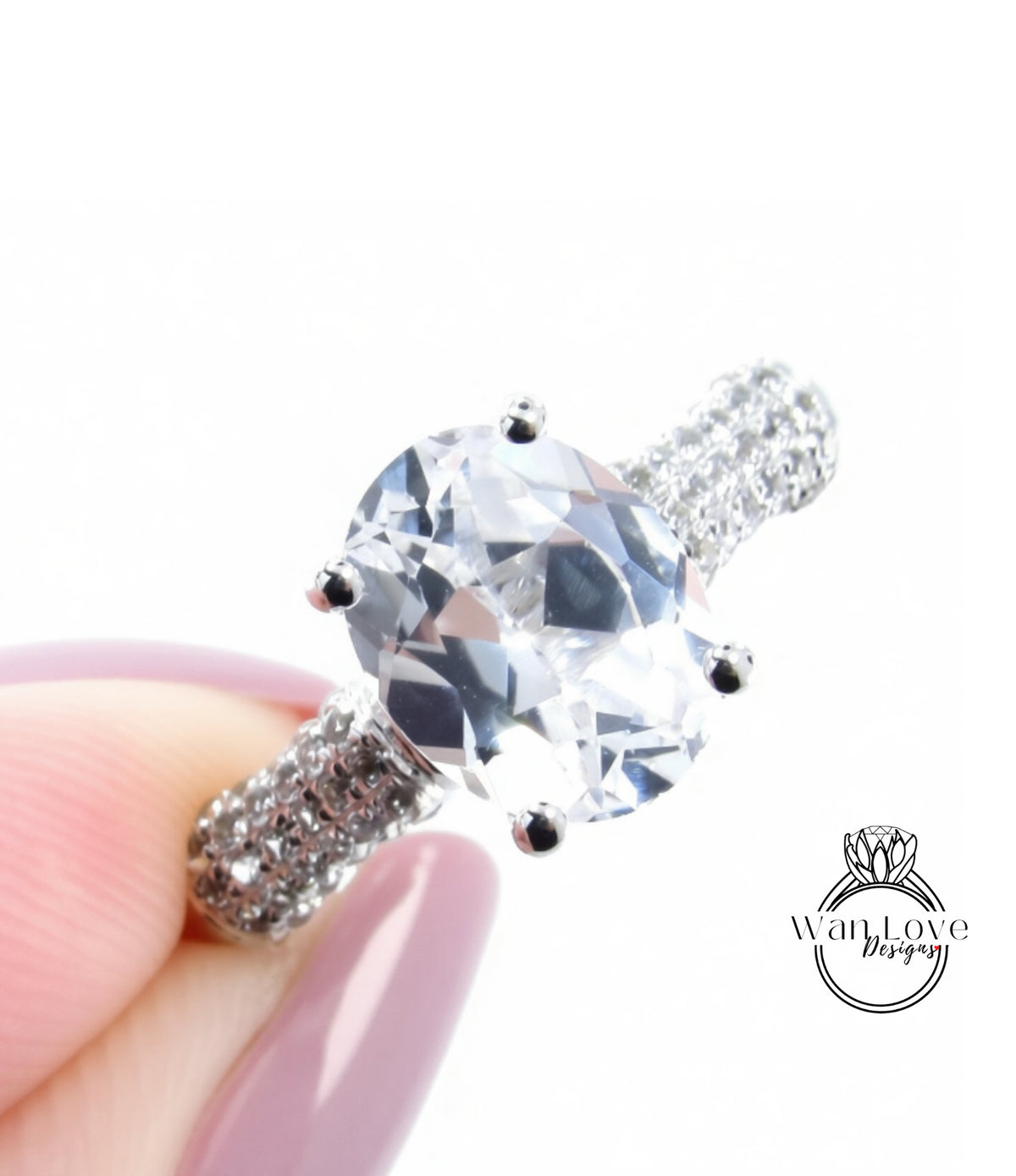 A close-up of a diamond engagement ring being held by a person's hand, with the ring's diamond set in a large oval-shaped stone surrounded by smaller diamonds.
