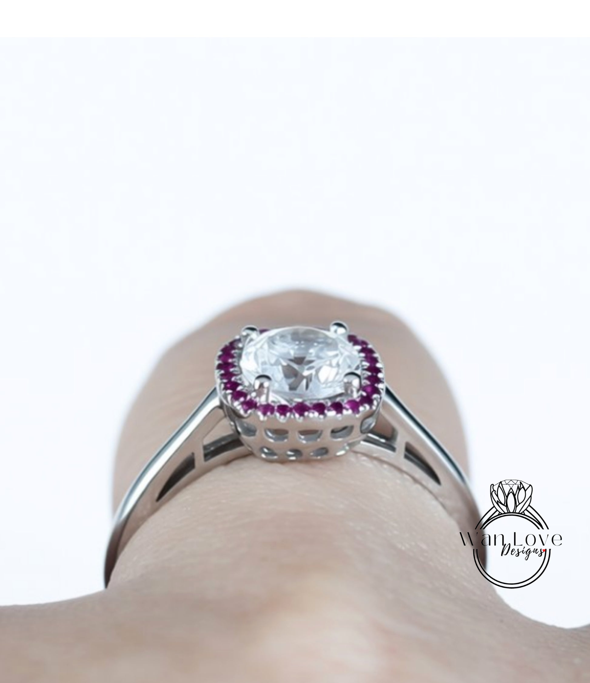 A close-up view of a person's hand wearing a silver ring with a large, clear gemstone at the center, surrounded by a halo of smaller, purple gemstones.
