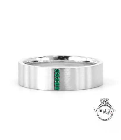 A silver-colored ring with a vertical band of green gemstones.