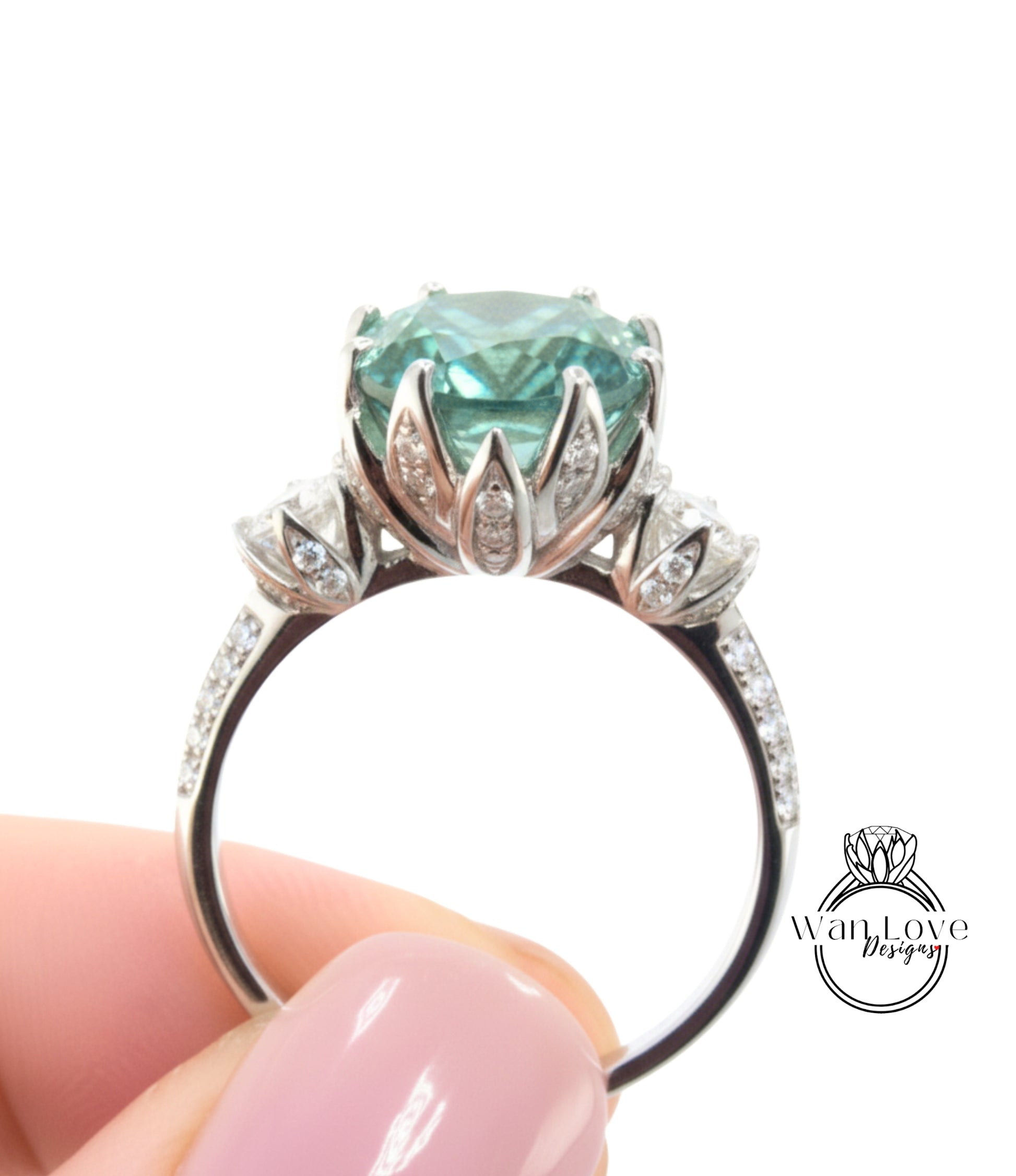A close-up of a person's hand holding a silver ring with a large, turquoise-colored gemstone, likely a diamond, surrounded by smaller diamonds.