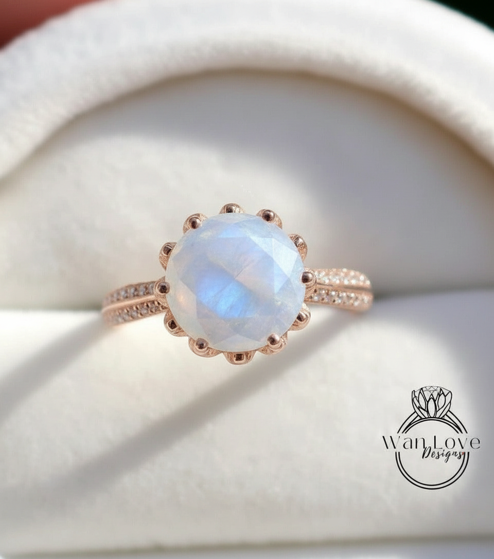 A close-up image of a rose gold ring with a large, round, blue moonstone as the centerpiece.