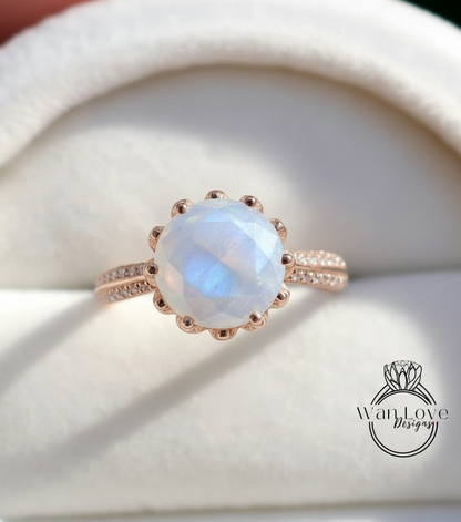 A close-up image of a rose gold ring with a large, round, blue moonstone as the centerpiece.