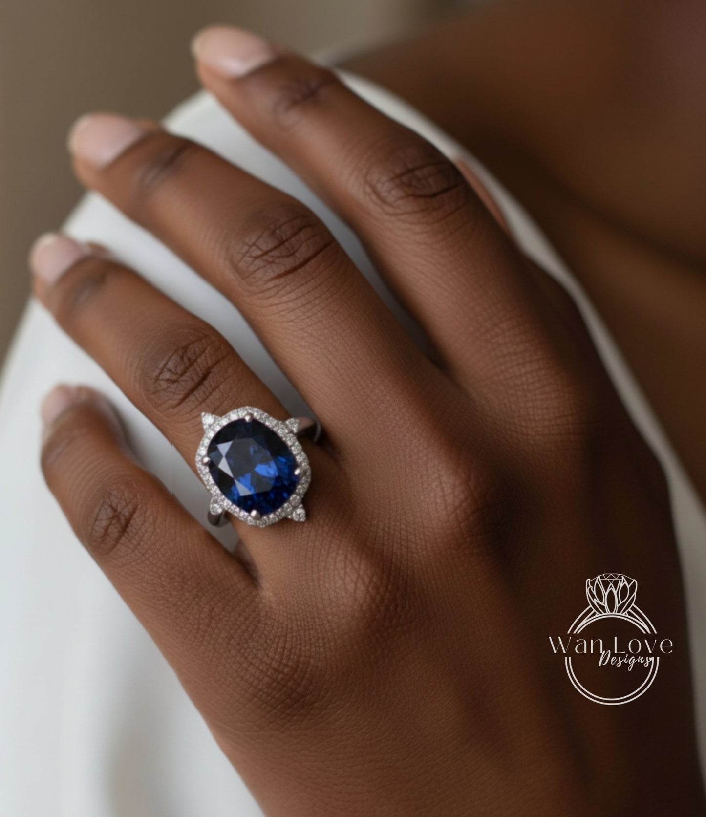 A close-up of a hand wearing a large, blue gemstone ring with a halo of smaller diamonds around it.