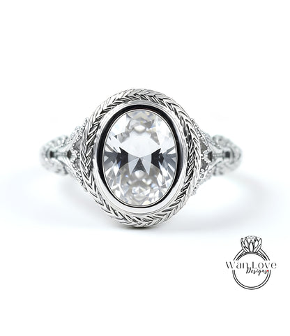 A close-up of a silver ring with a large oval-shaped gemstone, possibly a diamond, set in a decorative metal band.