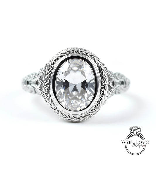 A close-up of a silver ring with a large oval-shaped gemstone, possibly a diamond, set in a decorative metal band.