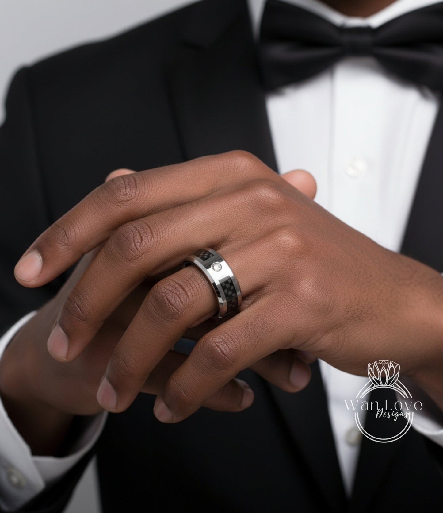 A close-up of a person's hand wearing a ring, with a black bow tie visible.