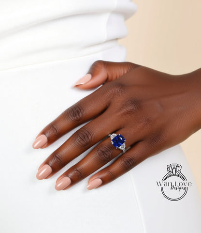 A close-up of a hand wearing a ring with a large blue gemstone, resting on a white surface.