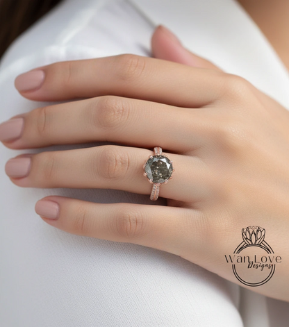 A close-up of a person's hand wearing a large, round, grey diamond engagement ring with a gold band.