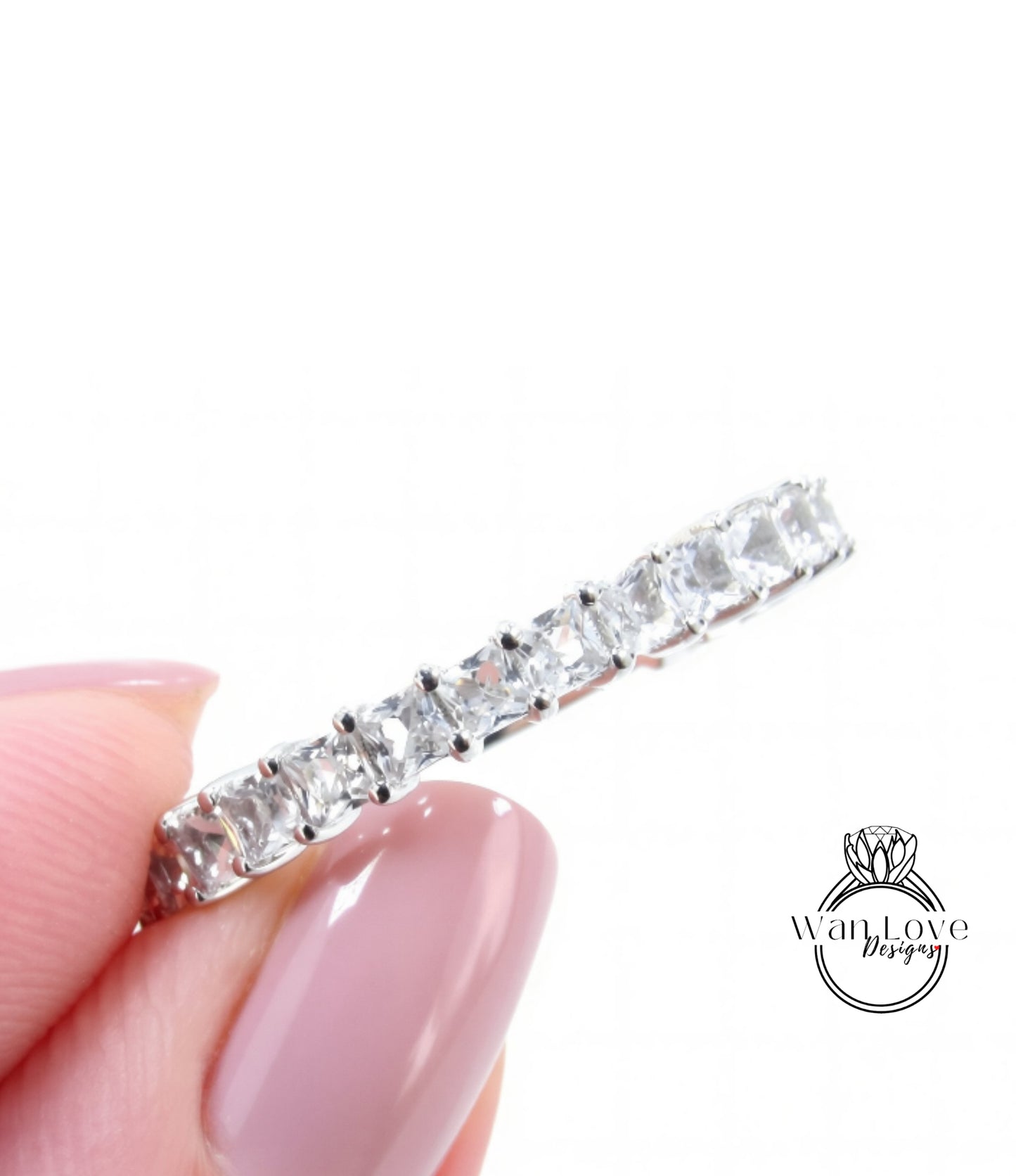 A close-up image of a person's hand holding a silver ring with a row of clear gemstones.