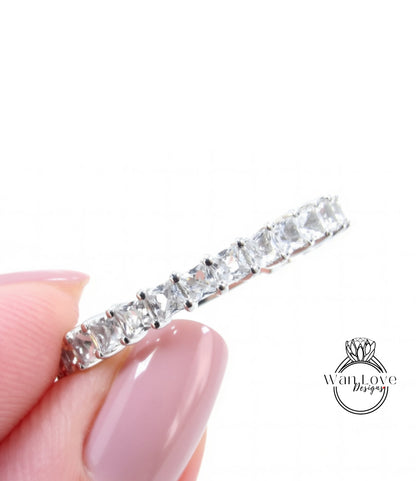 A close-up image of a person's hand holding a silver ring with a row of clear gemstones.