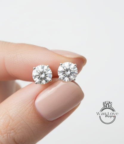 A close-up image of a person's hand holding a pair of diamond earrings against a white background.