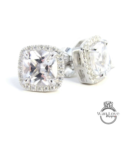 A pair of elegant earrings with large, clear gemstones set in a halo of smaller diamonds, creating a sparkling and luxurious appearance.