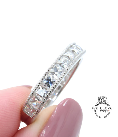 A close-up image of a person's hand holding a silver ring with a row of clear gemstones.