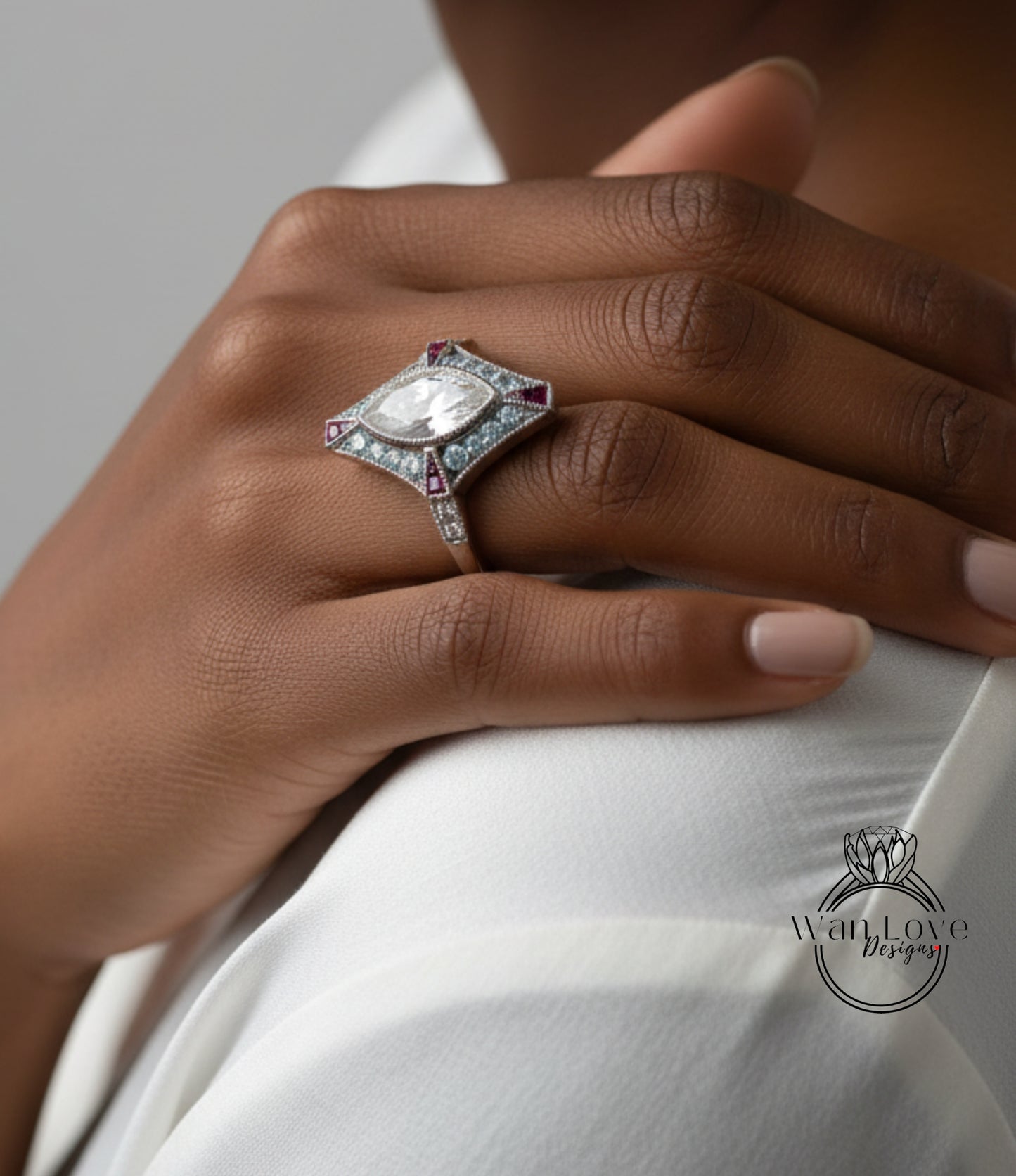 A close-up of a person's hand wearing a ring with a large gemstone, resting on a white shirt.