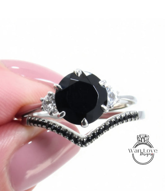 A close-up image of a person's hand holding a silver ring with a large black gemstone and smaller gemstones.
