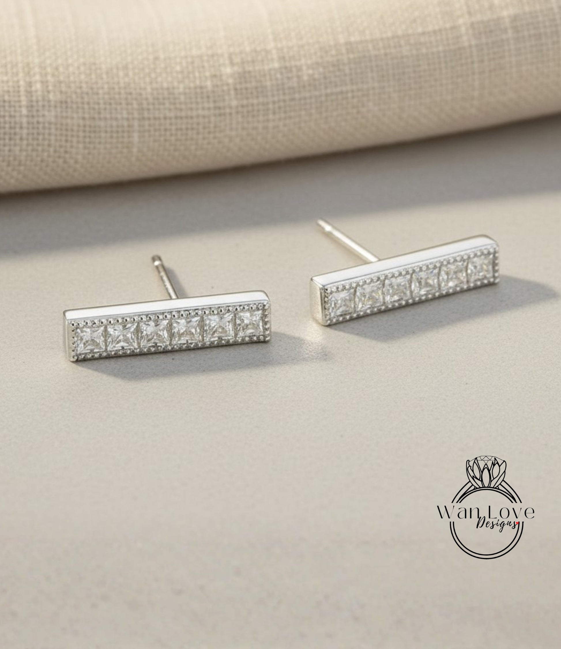 A pair of silver earrings with a row of small diamonds on the front, resting on a beige surface.