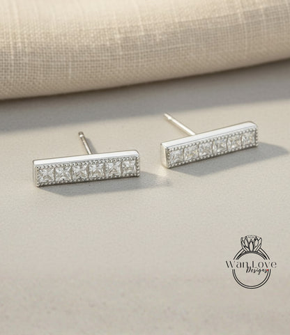 A pair of silver earrings with a row of small diamonds on the front, resting on a beige surface.