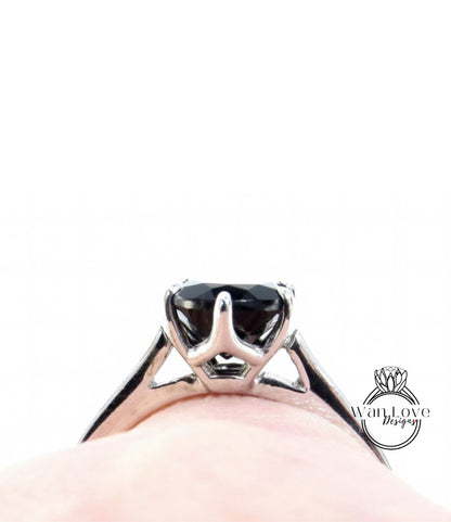A close-up view of a silver ring with a large black gemstone, possibly a diamond, set in the center of the band.