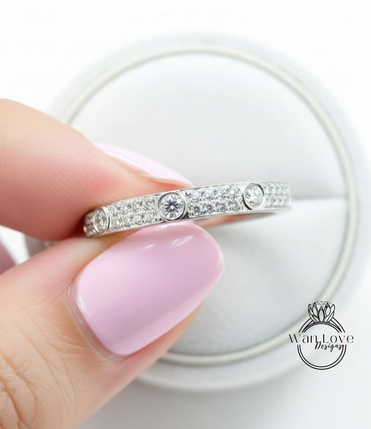 A close-up of a person's hand holding a diamond ring with a sparkling diamond band.