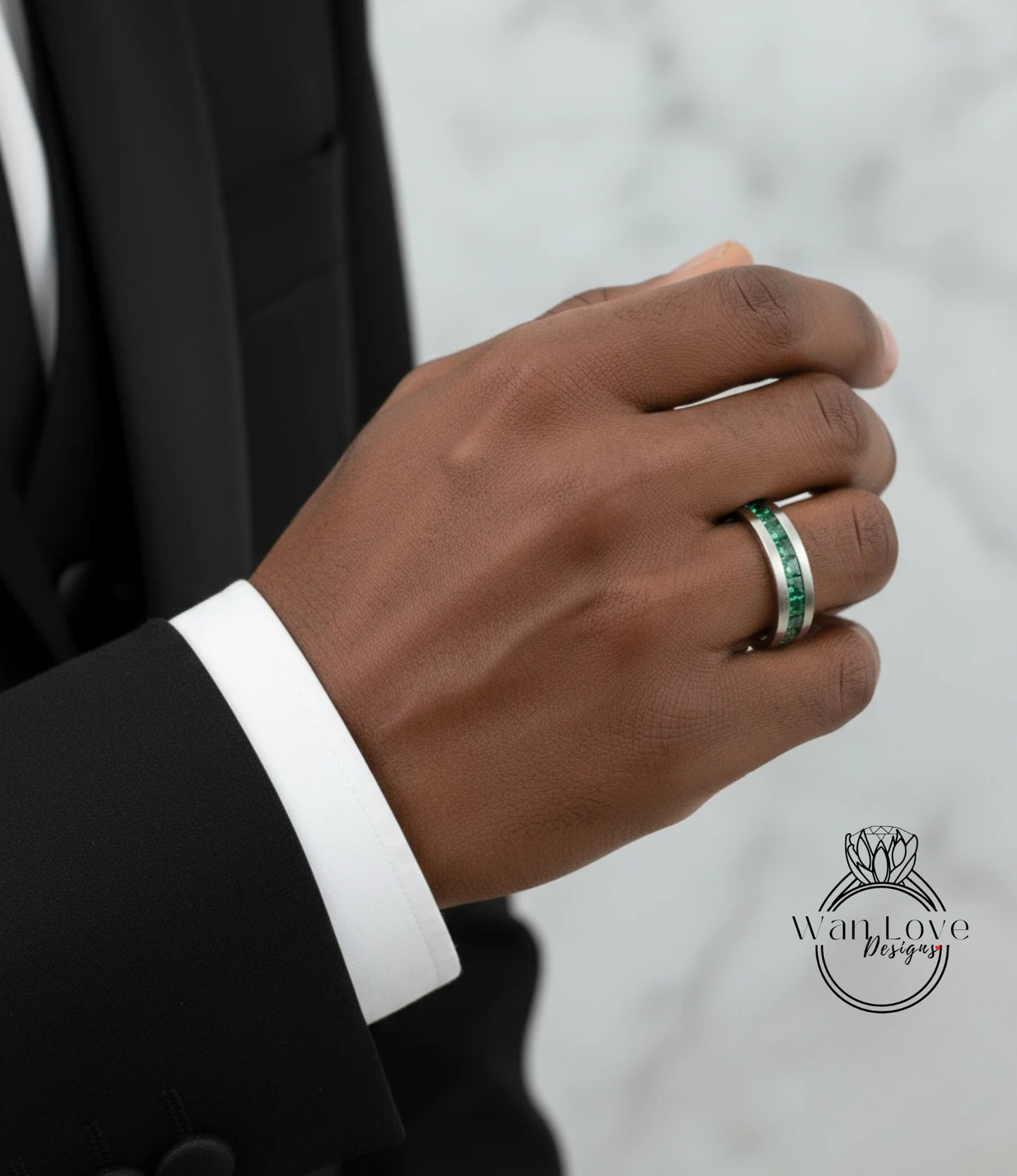 A close-up of a person's hand wearing a ring with a green gemstone, wearing a black suit jacket.