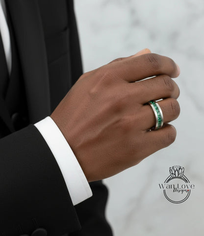 A close-up of a person's hand wearing a ring with a green gemstone, wearing a black suit jacket.