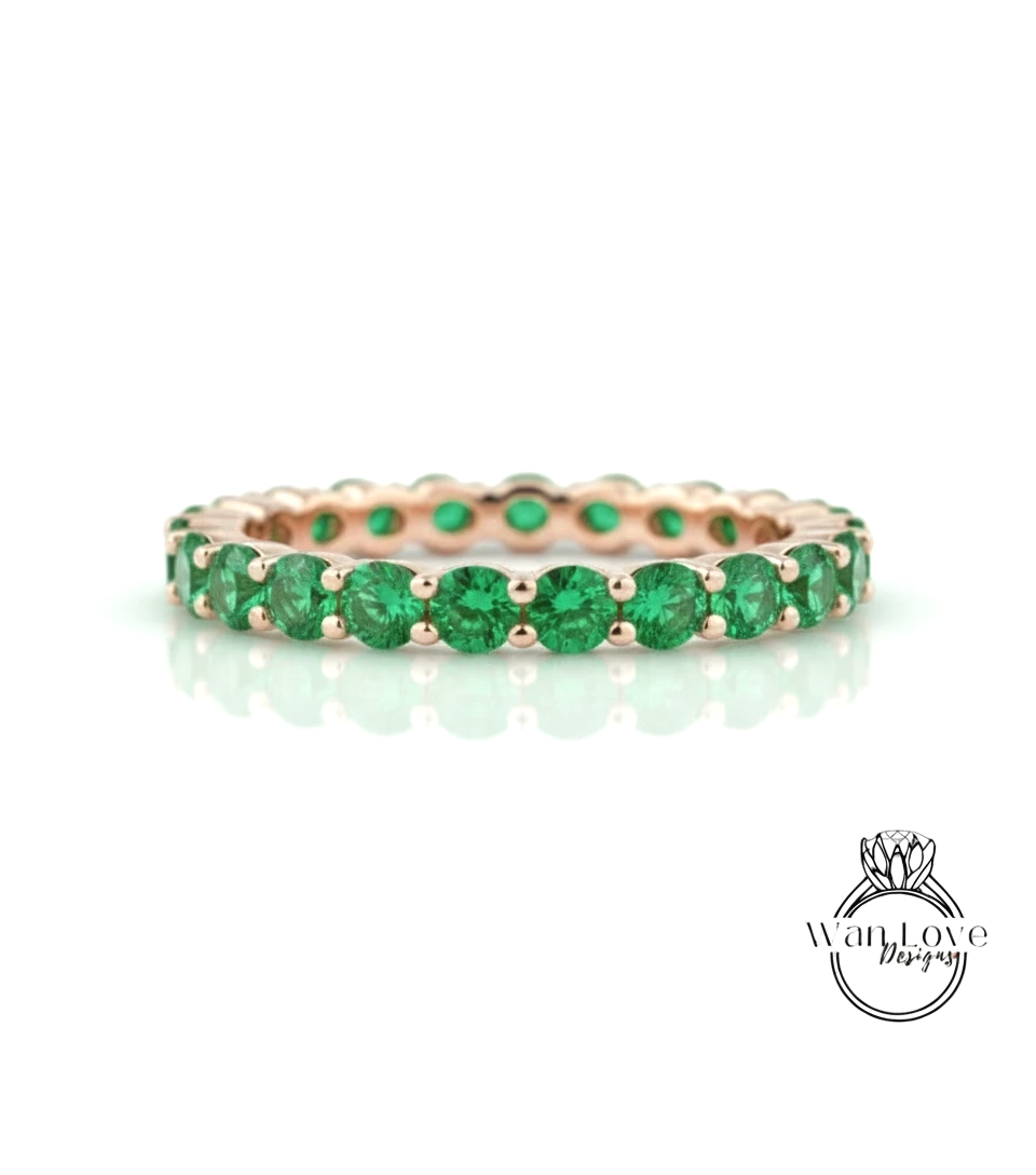 A gold ring with a row of green gemstones, likely emeralds, set in a delicate band.