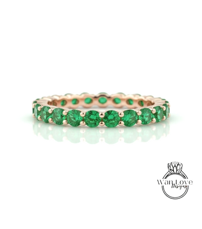 A gold ring with a row of green gemstones, likely emeralds, set in a delicate band.