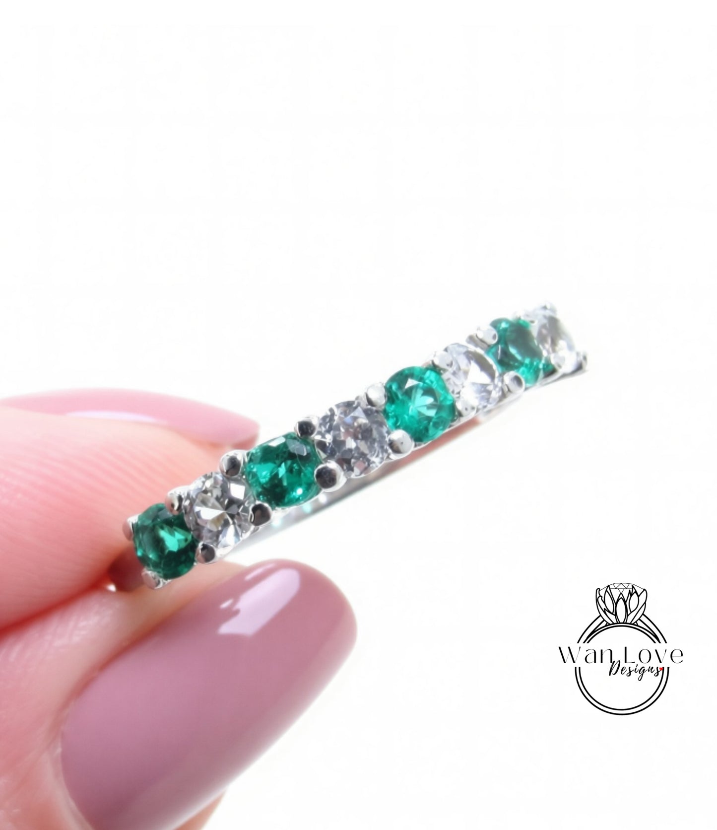 A close-up image of a person's hand holding a ring with a row of green and white gemstones.